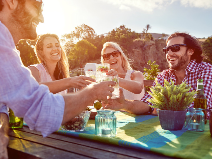 Group of friends toasting to a celebration with drinks while hanging out at a restaurant on a rooftop terrace
